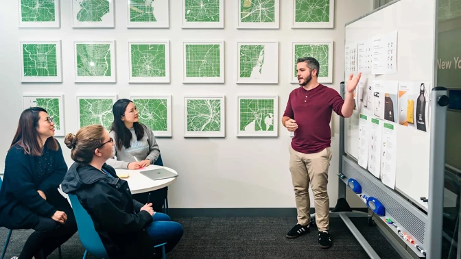 a person standing in front of a whiteboard with a person pointing at it